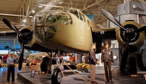 A vintage bomber aircraft on display in a museum, with two life-sized military figures nearby.