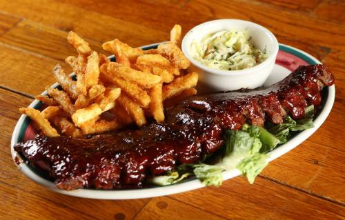 A plate of BBQ ribs with a side of crispy fries and coleslaw, served on a wooden table.