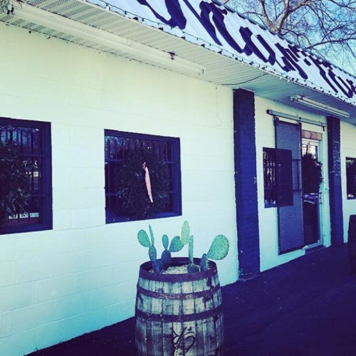 Exterior of a building with a light green wall, black windows, and a barrel planter with cacti in front.