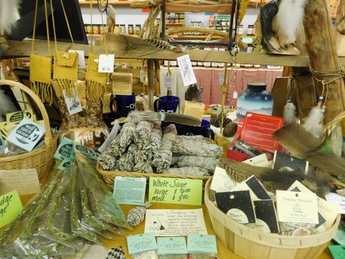 A display of various natural products, including sage bundles, feathers, and handmade items, in a cozy shop setting.