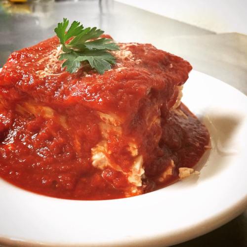 A serving of lasagna topped with marinara sauce and a sprig of parsley on a white plate.