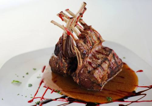 A beautifully plated rack of lamb with a rich sauce and decorative drizzle, garnished with herbs.