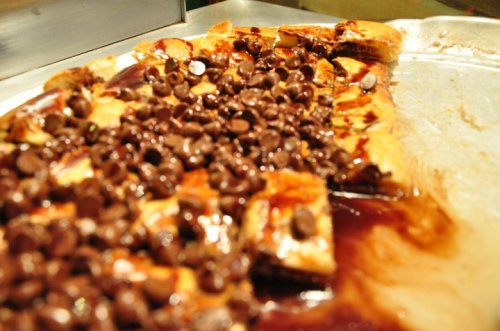 A tray of dessert featuring layers of pastry topped with chocolate chips and a glossy chocolate sauce.