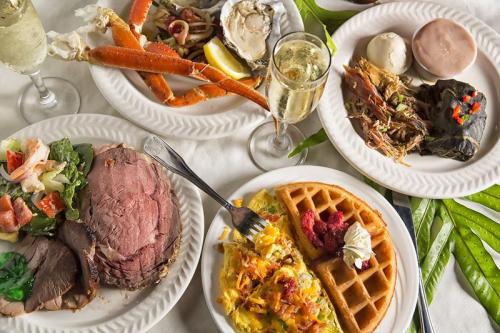 A table spread with various seafood dishes, prime rib, salad, an omelet, a waffle, and glasses of champagne.