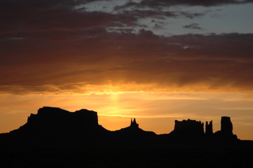 Silhouette of rock formations against a vibrant sunset with clouds in the sky.