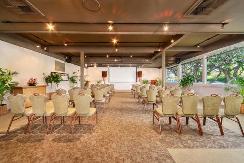 A spacious conference room set up with rows of chairs facing a screen, surrounded by plants and natural light.