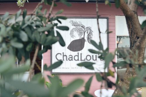 Sign for ChadLou's, a coffee house and ice cream shop, partially obscured by greenery.