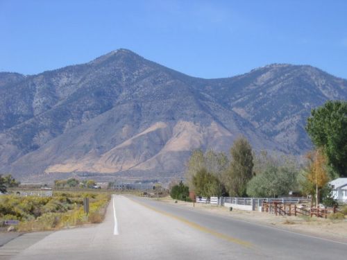 A scenic view of a wide road leading towards majestic mountains under a clear blue sky.