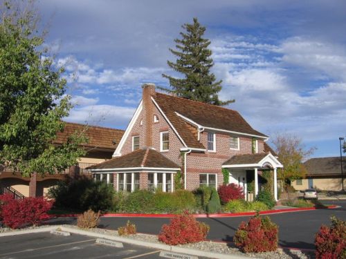 A charming brick house with a sloped roof, surrounded by colorful autumn foliage and a clear blue sky.