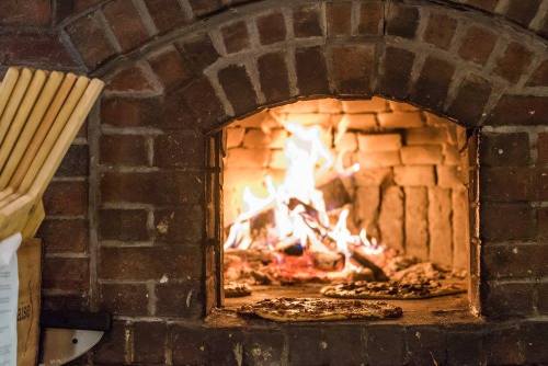 A brick oven with a roaring fire, showcasing glowing embers and a pizza baking on the stone floor.