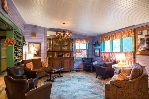 Cozy living room with purple walls, vintage furniture, a rug, and large windows, featuring warm lighting and decorative accents.