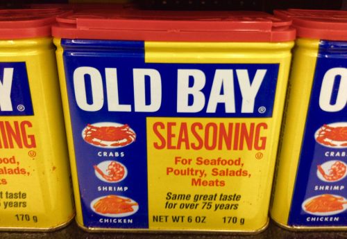 A can of Old Bay seasoning, featuring crabs, shrimp, and chicken, with a bright yellow and blue design.
