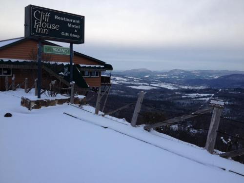 Snow-covered landscape with a sign for Cliff House Inn, overlooking distant hills and valleys under a cloudy sky.