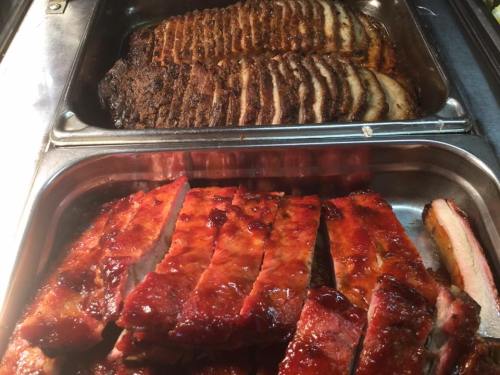 Two trays of cooked meats: one with sliced, seasoned beef and another with glazed, barbecued ribs.