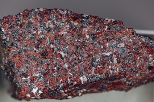 Close-up of a textured rock featuring a mix of red, black, and gray minerals with a crystalline appearance.