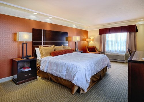 A cozy hotel room featuring a queen bed, bedside tables, lamps, and a window with curtains. Warm color scheme.