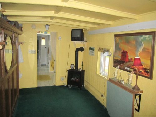 A cozy, yellow room with a green carpet, featuring a vintage TV, a painting, and a small stove.