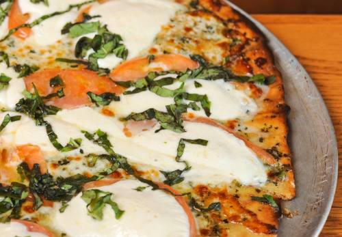 A close-up of a pizza topped with mozzarella, fresh basil, and slices of tomato on a golden crust.