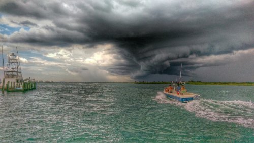 A boat speeds across a choppy sea under dark, ominous storm clouds, with a lighthouse in the background.