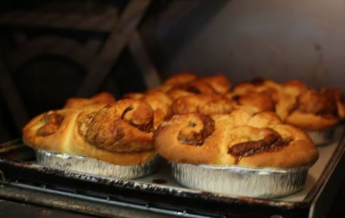 Freshly baked cinnamon rolls in aluminum trays, golden brown and fluffy, cooling in an oven.