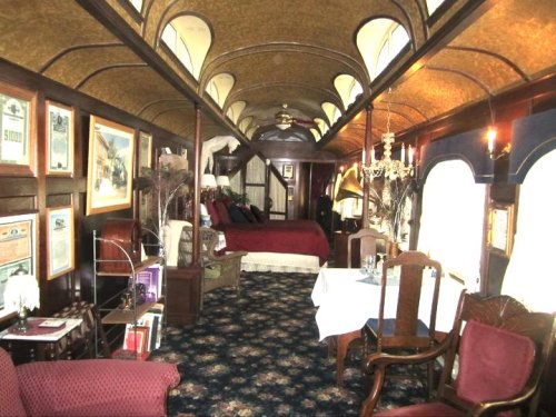 Luxurious vintage train car interior with a bedroom, dining area, and elegant decor, featuring rich colors and ornate details.