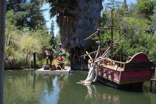 A scenic view of a small boat named "Joshua" docked by a lush, green area with two figures on a nearby platform.