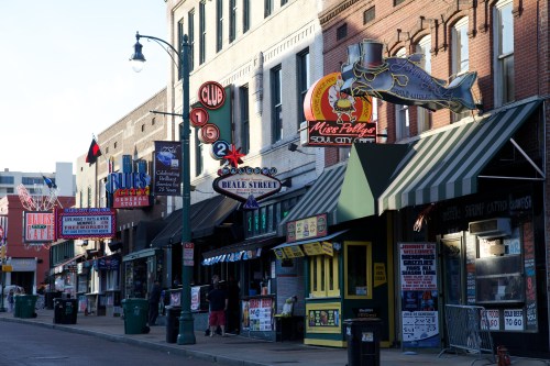 A vibrant street scene featuring colorful storefronts and neon signs along Beale Street, with people walking by.