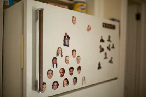A white refrigerator covered with various small face magnets arranged in clusters.