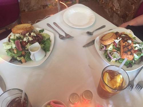Two plates of colorful salads with grilled salmon and bread, accompanied by drinks on a table.