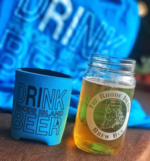 A blue koozie with "DRINK RHODE ISLAND BEER" next to a mason jar filled with beer and mint leaves.