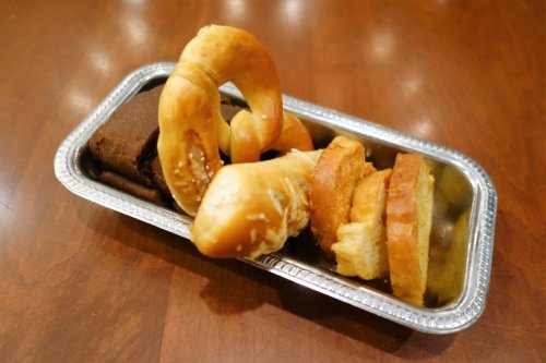 A metal tray with a variety of baked goods, including pretzels and slices of sweet bread.