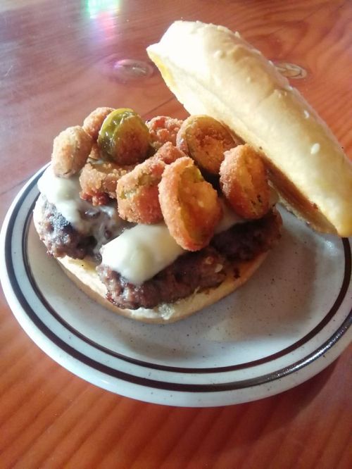 A hearty burger topped with fried pickles and jalapeños on a toasted bun, served on a plate.