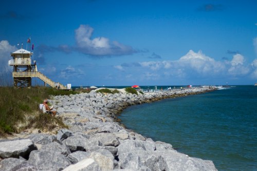 A lifeguard tower overlooks a rocky shoreline and calm blue waters under a partly cloudy sky.