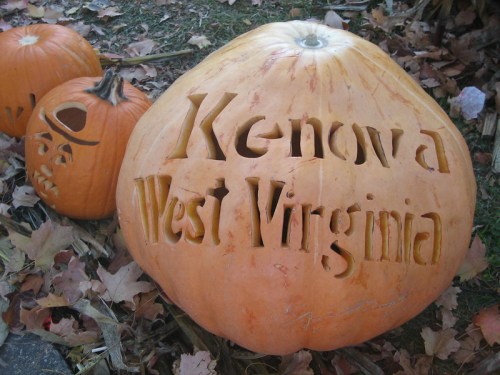 A large carved pumpkin displaying "Kenova West Virginia," surrounded by smaller pumpkins and autumn leaves.