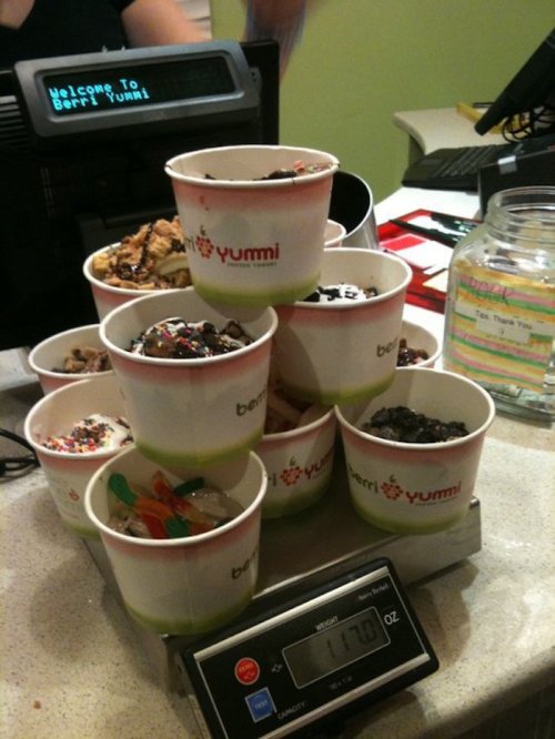 A stack of colorful dessert cups filled with various toppings on a scale at a frozen yogurt shop.