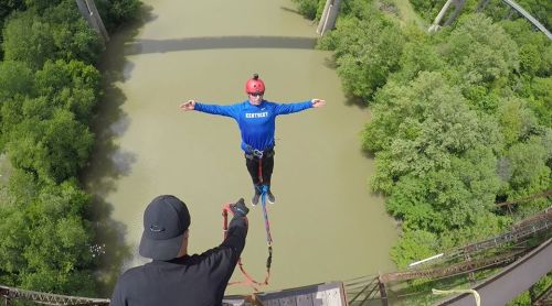 A person bungee jumping from a bridge, arms outstretched, with a lush green landscape and river below.