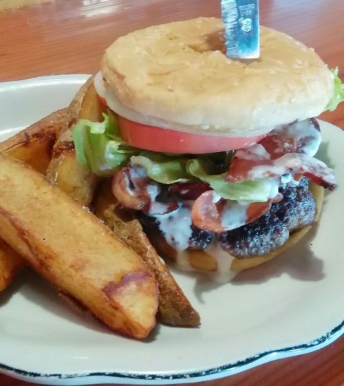 A juicy burger with bacon, lettuce, and tomato, served with crispy potato wedges on the side.