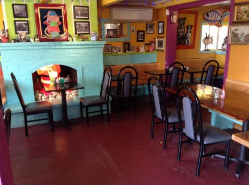 Colorful restaurant interior with tables, chairs, and a decorated fireplace. Walls adorned with various framed pictures.