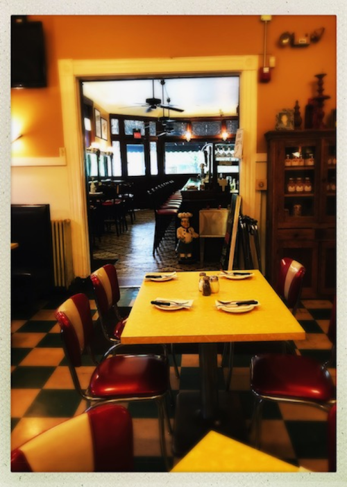 A cozy restaurant interior with a yellow table, red chairs, and a view of the dining area in the background.