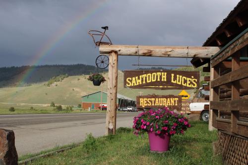 Sign for Sawtooth Luce's Restaurant with a rainbow in the background and colorful flowers in a pot.