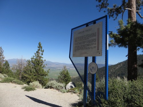 Sign for Carson Valley with a scenic view of the valley and mountains in the background, surrounded by trees.