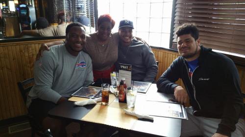 Four people sitting at a table in a restaurant, smiling and posing for the photo with menus in front of them.