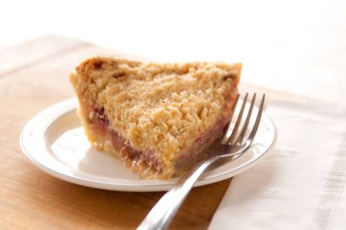 A slice of crumb-topped pie on a white plate with a fork, resting on a wooden surface.