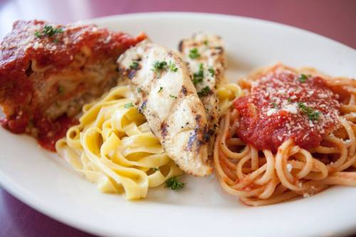 A plate of pasta with marinara sauce, grilled chicken, and fettuccine, garnished with parsley.