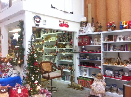 A cozy shop filled with holiday decorations, vintage items, and a small Christmas tree, creating a festive atmosphere.