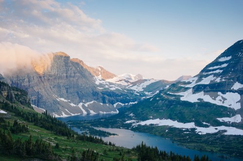 A scenic mountain landscape with snow-capped peaks, a serene lake, and lush green valleys under a clear sky.