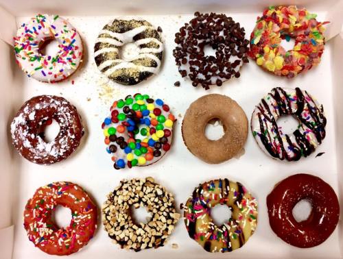 A box of assorted donuts with various toppings, including sprinkles, chocolate, and colorful candies.