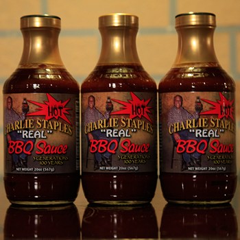 Three bottles of "Charlie Staples 'Real' BBQ Sauce," each labeled with a hot sauce graphic and a photo of the brand's founder.