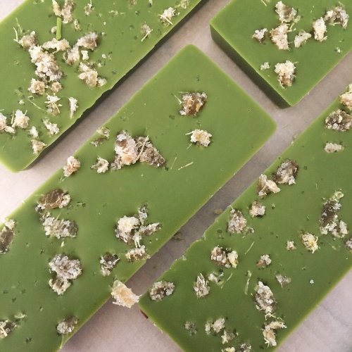 Four green soap bars topped with small pieces of dried herbs on a light background.