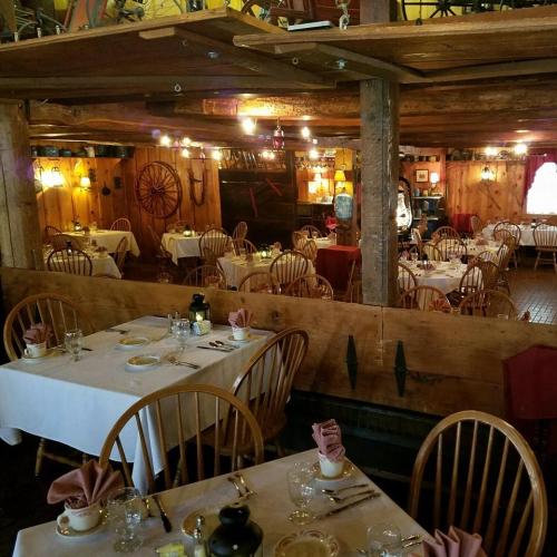Cozy restaurant interior with wooden tables, chairs, and warm lighting, set for dining with napkins and tableware.